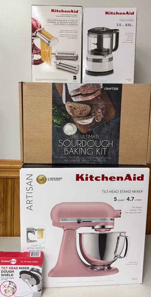 RAFFLE #568 features a Pink 5Qt KitchenAid Stand Mixer with attachments and a Sourdough Starter Kit, all packaged and displayed against wood paneling—an ideal prize for any kitchen enthusiast.