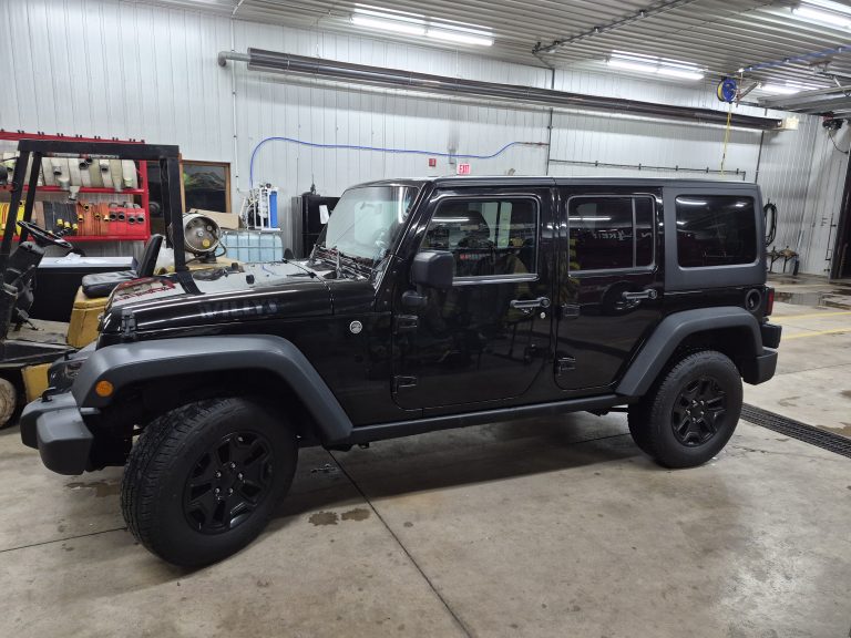 A black 2018 Jeep Wrangler Unlimited Willy's 4x4 Hardtop—Raffle #710, with sales tax and tags included plus $500 to numbers above and below the winner—is parked in a well-lit garage, surrounded by tools and equipment, ready as a raffle prize.